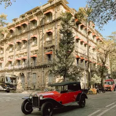 A beautiful red vintage car from a bygone era, pictured on the streets of South Bombay. It's a ride back in time, showcasing the elegance of classic automotive history.