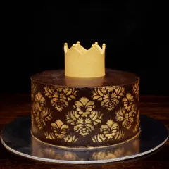 A royal chocolate truffle cake for a special occasion. This egg-free cake features a rich chocolate ganache with a gold damask stencil pattern and is topped with a golden crown. It's filled with fresh strawberries inside.