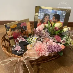A hamper as beautiful as their love story. This wicker basket arrangement features personalized photo frames, custom-decorated jars, and a beautiful assortment of artificial flowers for a lasting memory.