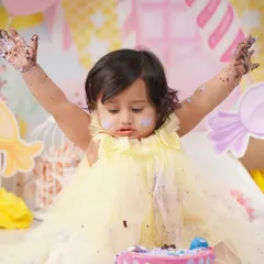 A baby girl throws her hands up in the air, covered in chocolate frosting during a wonderfully messy Candyland-themed cake smash.