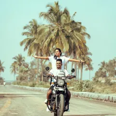 A classic "king of the world" pose on a Royal Enfield, riding down a palm-tree-lined road. This shot is all about freedom, adventure, and starting a new journey together.