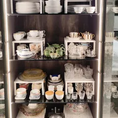 This beautifully lit crockery unit showcases a variety of tea sets and glassware. By using risers and grouping sets together, the collection is not only organized and safe but also visually stunning.