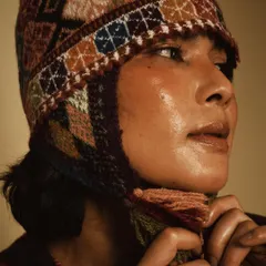 A close-up portrait highlighting the intricate knitwear and the model's glowing skin. The warm tones and soft focus create an intimate and cozy feeling, perfect for this slow fashion brand.