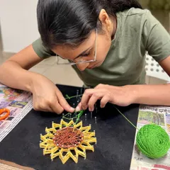 Deep in concentration, this participant meticulously weaves green and yellow string to form the petals of a beautiful sunflower.
