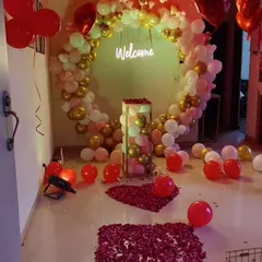 A grand welcome setup featuring a large circular balloon arch in white and gold. The entrance path is decorated with rose petals, leading to a 'Welcome' neon sign inside the arch.