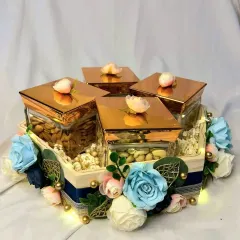 This elegant dry fruit box is a popular choice for trousseau gifting. The square glass jars with rose gold lids are arranged in a floral-decorated wooden tray, combining modern style with a touch of tradition.