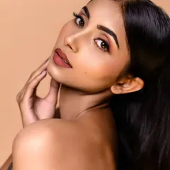 A clean and classic beauty shot against a solid beige backdrop. The lighting is soft and even, perfectly capturing the natural-looking makeup and smooth skin texture.