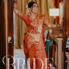 A beautiful portrait of the bride, Jestha, making a joyful entrance. Her radiant smile and stunning red and gold Kanjeevaram saree capture the essence of a happy South Indian bride.