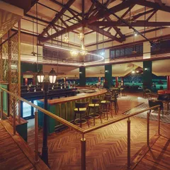 From this angle at the KGA bar, you can see how uplighting the stunning wooden ceiling trusses makes the entire space feel larger and more grand. The contrast between the illuminated ceiling and the moody, low-lit seating areas creates a dynamic and inviting ambiance.