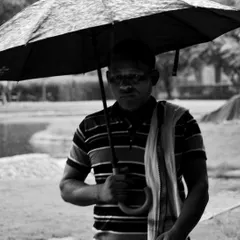 A black and white street portrait of a man holding an umbrella. This moody, monochromatic shot focuses on the subject's expression and the atmosphere of a rainy day.