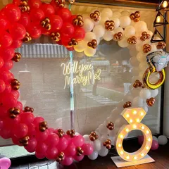 A heart-shaped balloon arch in red, pink, and white for a proposal or ring ceremony. The 'Will you Marry Me?' sign and diamond ring balloon add a fun and romantic touch to the decor.
