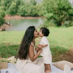 A sweet kiss between mother and son. This tender moment captures the special bond they share, set against the backdrop of their lovely lakeside picnic.