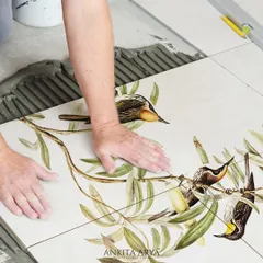 The installation process of custom-printed ceramic tiles. Each tile is a piece of a larger picture, coming together to create a seamless mural of birds perched on olive branches.