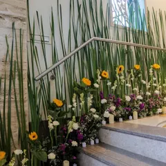 I love transforming overlooked spaces like staircases into beautiful features. This arrangement uses tall green stalks, bright sunflowers, and other fresh flowers to create a natural and artistic floral installation.