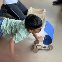 A camper gets down on the floor to test the sail car he built, learning about wind power in the most direct way possible.