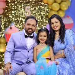 A classic family photo taken at a 5th birthday party. The parents and their daughter are all smiles against a festive backdrop, creating a perfect memory of this important milestone.
