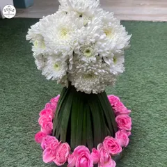 A beautiful floral creation featuring a base of folded green leaves, a ring of pink roses, and a crown of white chrysanthemums. This is a wonderful example of a structured yet soft centerpiece.