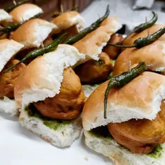 A detailed look at our homemade Vada Pav, with a spiced potato fritter tucked inside a soft pav bread, layered with green chutney and topped with a fried green chili.