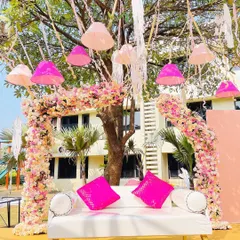This special seating area for a Haldi ceremony is set under a tree decorated with hanging lampshades. The floral arch and bright pink cushions create a cheerful and picturesque spot for the couple.