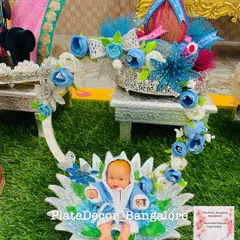 This is a custom-designed baby shower platter with a blue floral theme. The centerpiece is a baby doll in a decorative cradle, surrounded by other gift items.