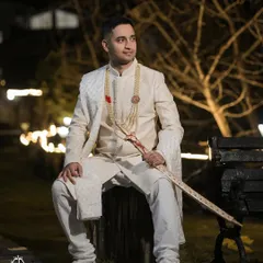 A full-length portrait of the groom seated outdoors at night. The lighting creates a dramatic, cinematic feel, highlighting his sharp attire.