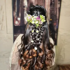 An elegant and modern hairstyle with intricate braids and soft curls, adorned with fresh flowers. This is a perfect look for an engagement or sangeet ceremony.