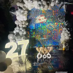 A full view of the glamorous silver-themed 27th birthday party. The combination of the iridescent sequin wall, the cloud-like balloon arch, and the glowing marquee numbers made the entire space feel like a VIP event.