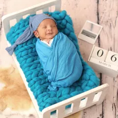 A sweet smile in his sleep. This cozy shot features a baby swaddled on a miniature bed, a perfect example of a classic, prop-based newborn portrait.