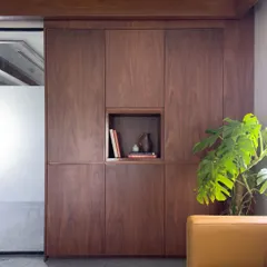 Detail of the custom, floor-to-ceiling walnut storage unit in an executive office. The seamless, handle-free design includes a central niche for display, combining practical storage with minimalist aesthetics.