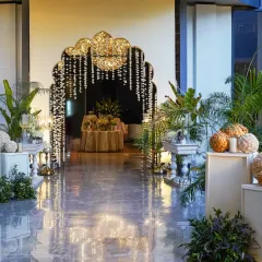 We designed this grand entrance with a floral-draped Mughal arch, framing a welcoming view of the event inside. The pathway is lined with tropical plants and classic pedestals, setting a tone of refined elegance.