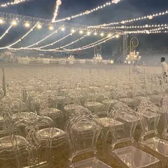 A glimpse of the venue during setup, with rows of elegant ghost chairs being arranged under a canopy of lights. This showcases the scale and precision of our event production.