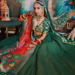 A regal bridal look in a stunning green lehenga with a colorful bandhani dupatta. The makeup is kept classic and glowing to complement the rich, royal colors of the outfit.