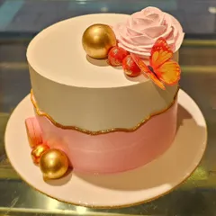 A minimalist and chic designer cake. The two-tone pink and white design is accented with a simple gold line, a delicate pink rose, edible gold spheres, and a butterfly for a touch of elegance.