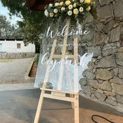 An elegant acrylic welcome sign for Liyansh's first birthday, topped with a beautiful arrangement of white roses.