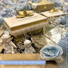 "Welcome little one with pure delight!" This baby announcement hamper features cherub figurines, a silver-plated shell dish, and an ornate box, all in a beautiful blue and white color scheme for a baby boy.