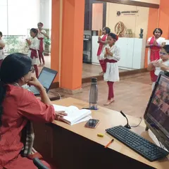 A guru instructs students in person while simultaneously managing an online session. This hybrid approach allows us to offer flexible learning options for Bharatanatyam, Kathak, and music classes.