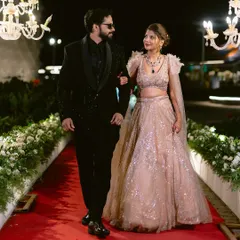 A glamorous couple makes their entrance on a classic red carpet, lined with pristine white floral arrangements. The overhead chandeliers add a touch of royal elegance to their reception walk.