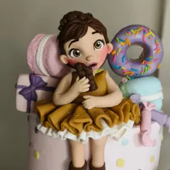 A detailed shot of the girl figurine from the Candyland cake. I focused on her joyful expression as she nibbles on a chocolate bar, surrounded by colorful, edible sweets like a donut and macaron.