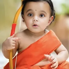 A close-up portrait of a baby boy dressed as Little Rama for Rama Navami. The focus is on his innocent expression and the simple, traditional attire.