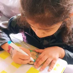 Look at the concentration on this little artist's face! We provide a variety of wooden cutouts and colorful markers so every child can create a unique piece. It's a wonderful activity for developing fine motor skills.