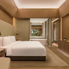Our rooms are designed to be your personal sanctuary. This suite features a king-sized bed, contemporary furnishings, and a view of the bathroom and greenery beyond.