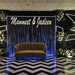 A chic and modern reception stage for Manmeet and Jasleen. The design features a dramatic black and white chevron floor, custom neon-style lighting, and elegant white floral arrangements for a high-impact, contemporary look.