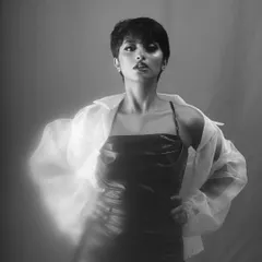 A confident black and white portrait of a model in a dark dress and a sheer white shirt. The soft, glowing effect around her adds a touch of ethereal drama to this fashion-forward shot.