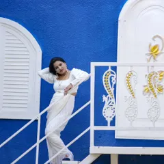 A stylish portrait of a woman in a white saree against a vibrant blue wall, taken during her birthday photoshoot.
