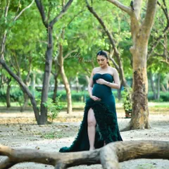 A solo portrait of an expectant mother in a lush green forest setting. The deep green of her gown complements the natural surroundings, creating a rich and vibrant pregnancy photograph.
