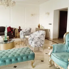 Another angle of this elegant living room, showcasing the mix of custom furniture pieces. A classic sofa is paired with modern patterned armchairs and a striking turquoise and gold Victorian-style chair. The white walls with decorative moulding provide a clean canvas that makes the colorful furniture stand out.