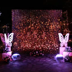 A dramatic rose-gold sequin wall set up outdoors for a marriage event, flanked by elegant white butterfly props for a touch of whimsy.