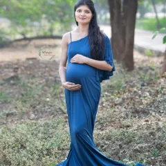 A graceful portrait in a beautiful blue gown. The one-shoulder design and long train add a touch of elegance to this outdoor maternity photo in the woods.