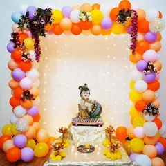 A Janmashtami decoration featuring a balloon arch in vibrant colors around a Krishna idol, with fairy lights adding a magical glow.