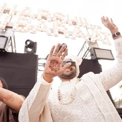 The groom shows off his mehendi, with the bride's initial creatively designed on his palm. This fun, candid shot captures a modern tradition and the festive spirit of the wedding.
